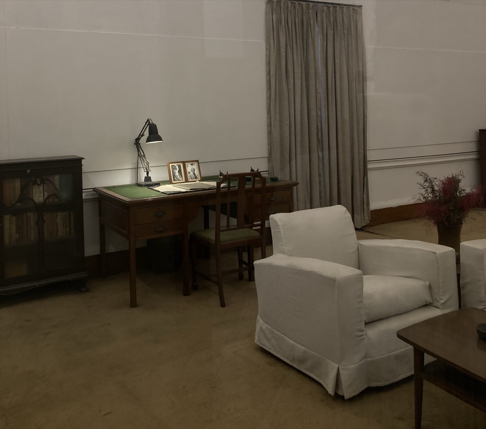 A wooden writing desk with an open notebook beneath a desk lamp in a quiet room